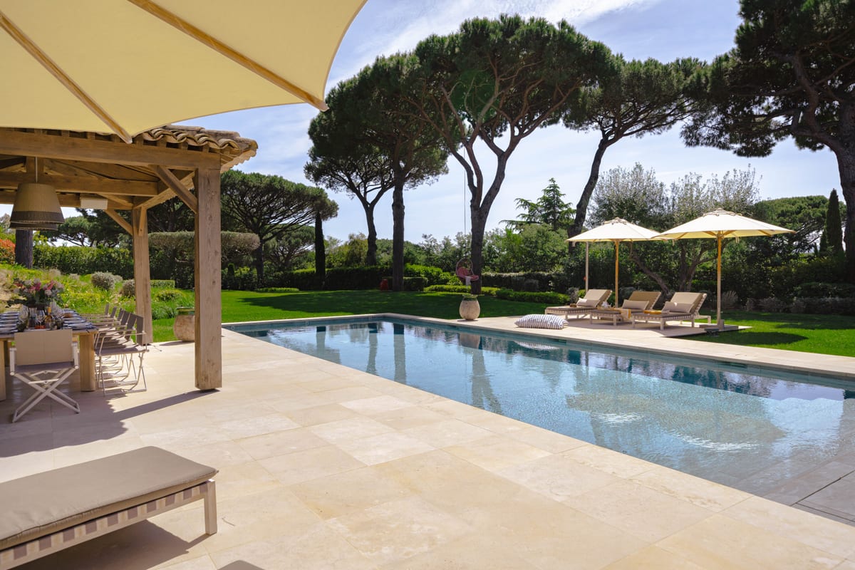 The pool seen from under a pergola, loungers along the far side.