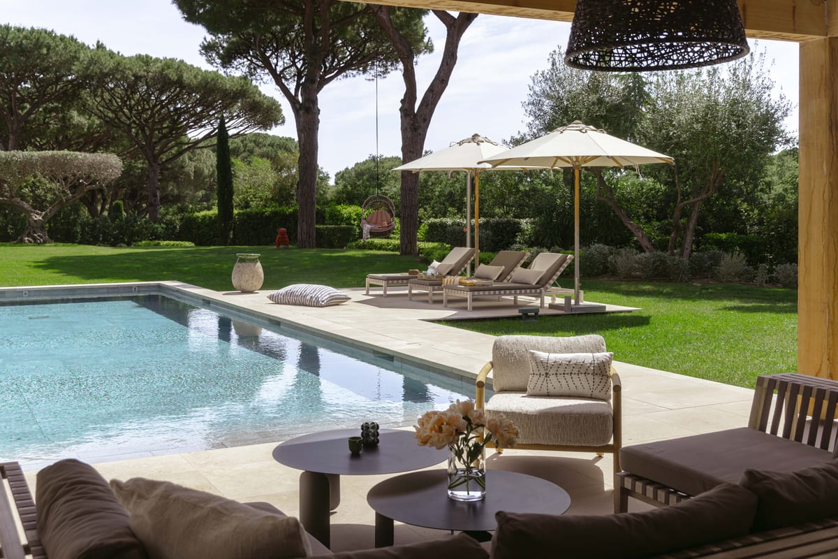 An outdoor sofa and low table beside the pool, loungers and umbrellas along the lawn.