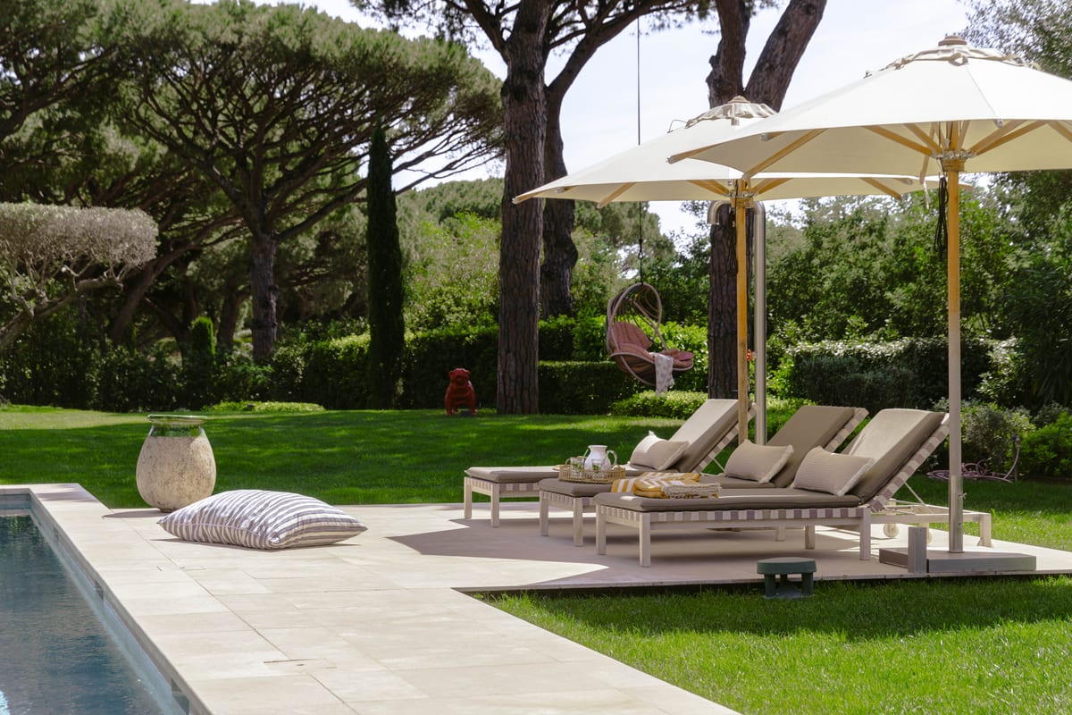 Loungers and a parasol at the edge of the pool, lawn and pines behind.