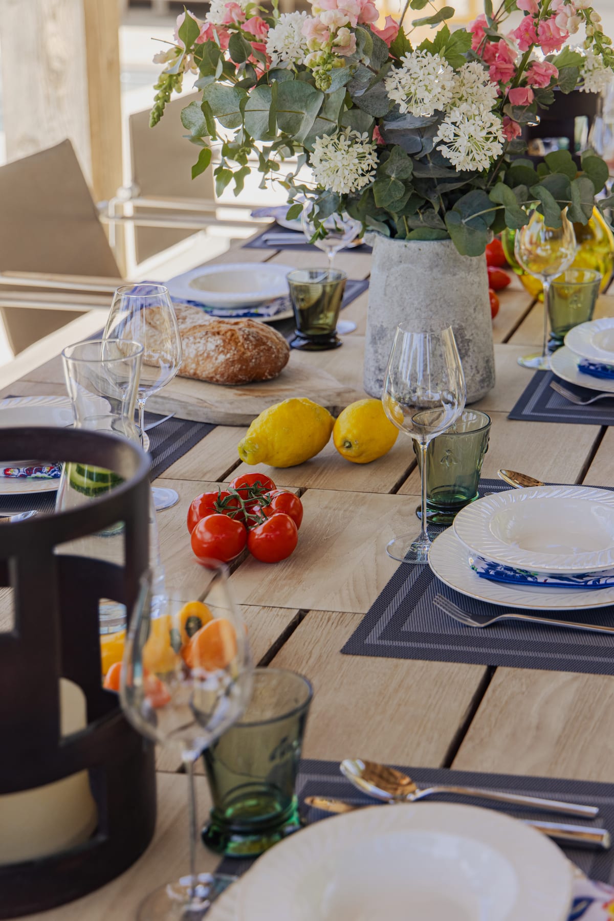 A table laid outdoors, close up: flowers, lemons, glassware and blue linen.