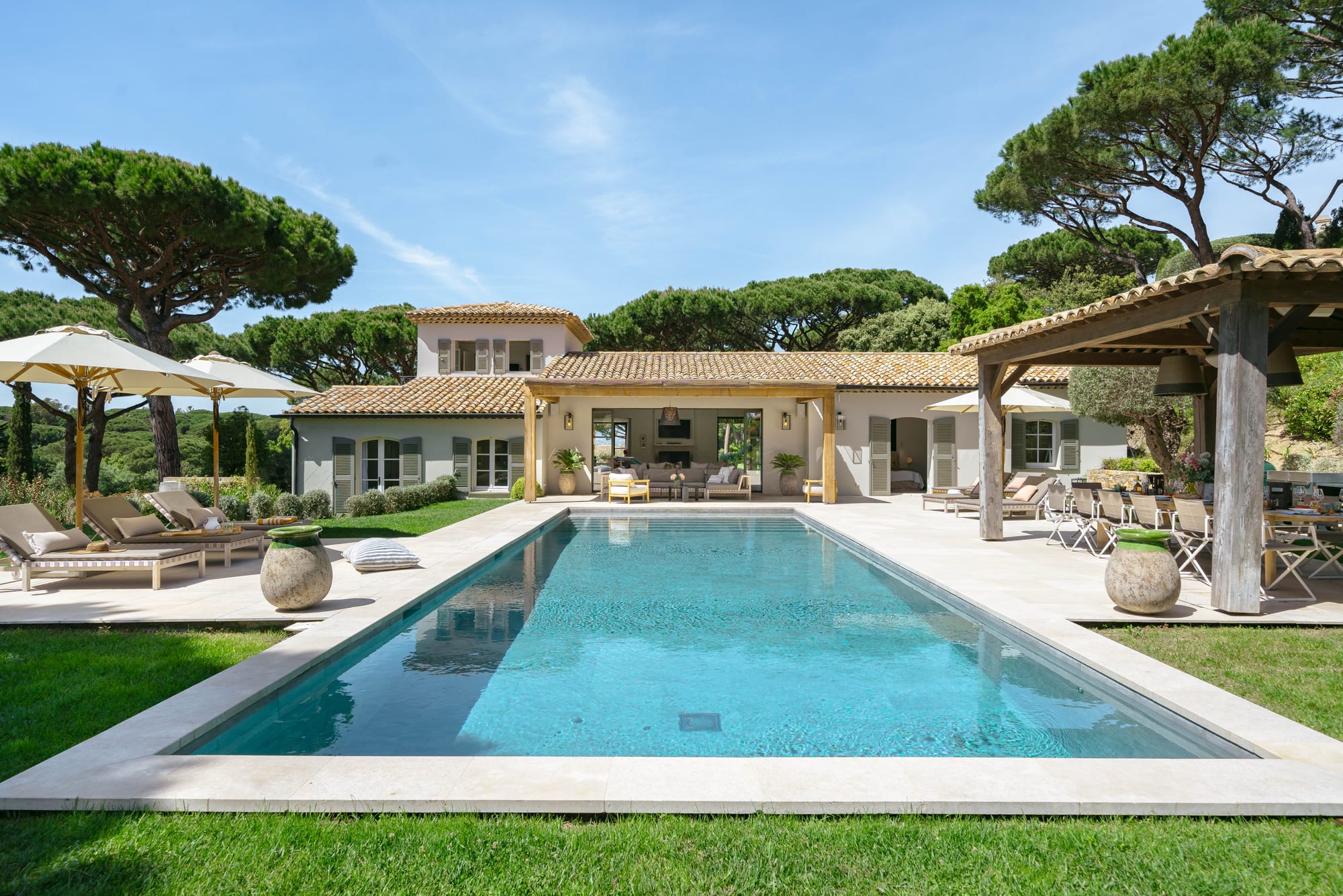The house seen across the pool, with pines on both sides and loungers along the near edge.