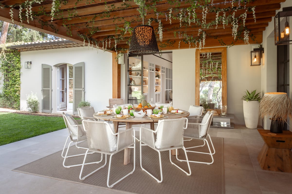 A table laid for lunch under the pergola, trailing plants along the beams, lawn to the left.