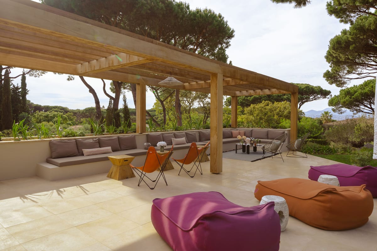 A long timber pergola sheltering a built-in sofa, low tables and floor cushions.
