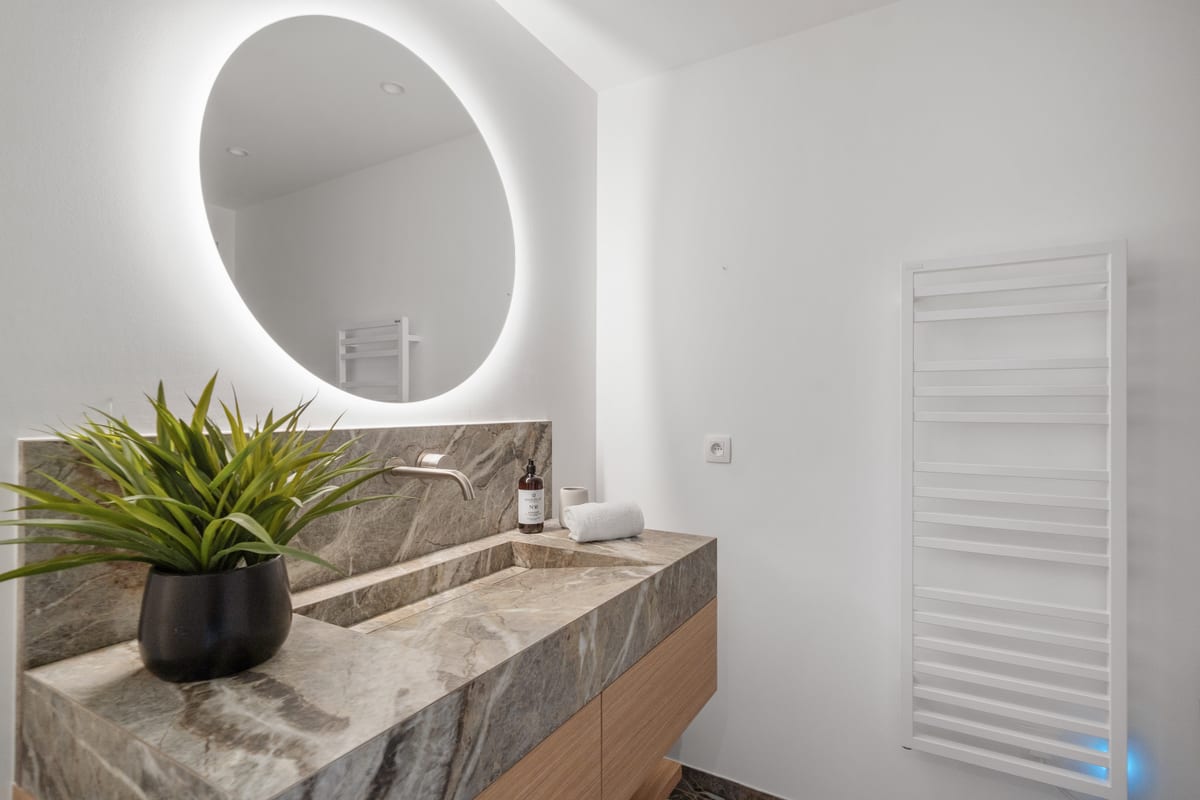A bathroom with a backlit round mirror above a stone vanity.