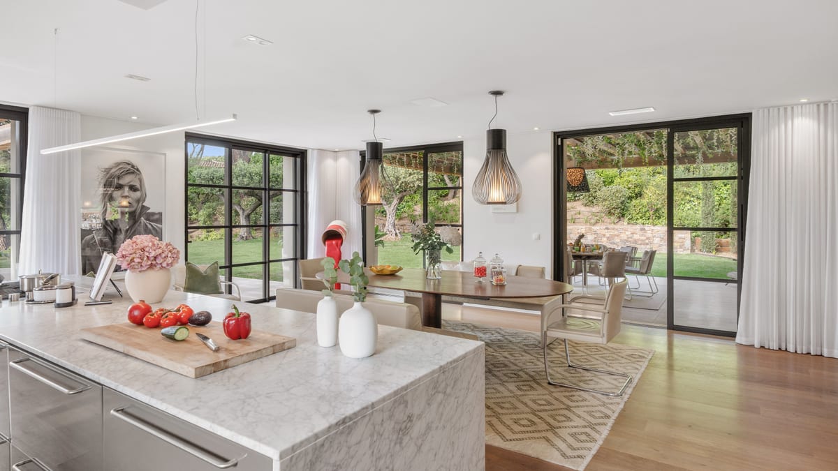An open kitchen with a stone island, pendant lights above it and a dining table beyond.