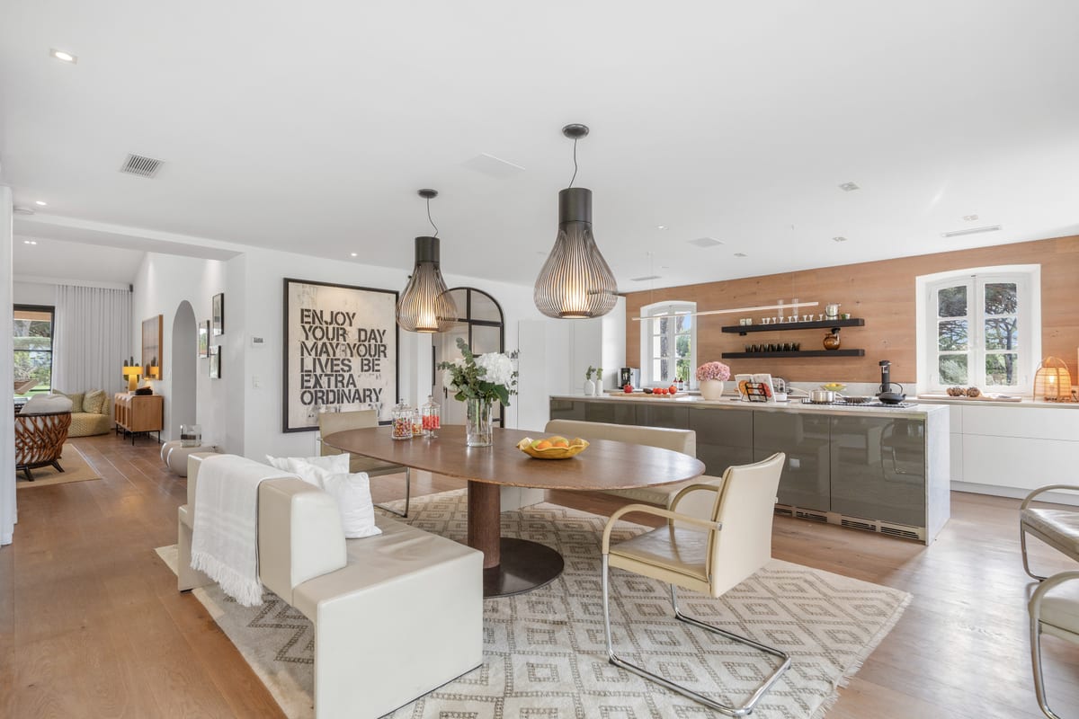 An open living room and kitchen under pendant lamps, with a dining table between them.
