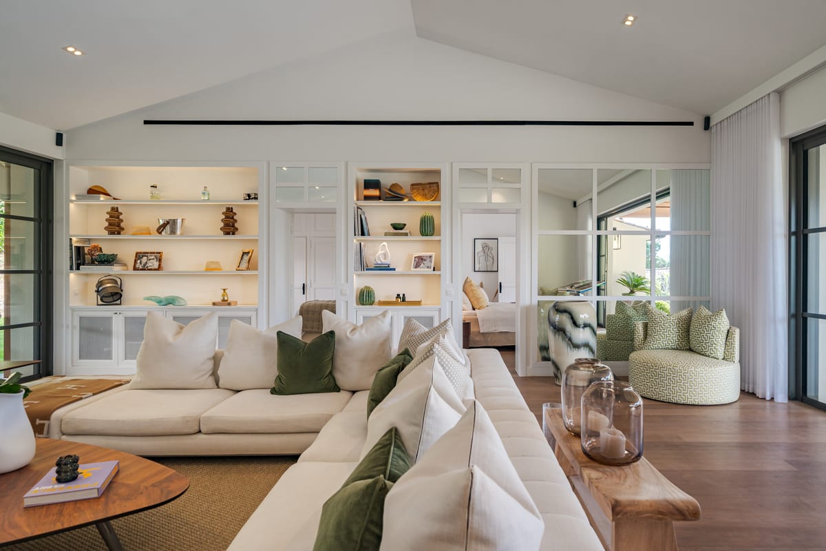 A living room under a pitched white ceiling, pale sofas, built-in shelving and glazed doors to the garden.