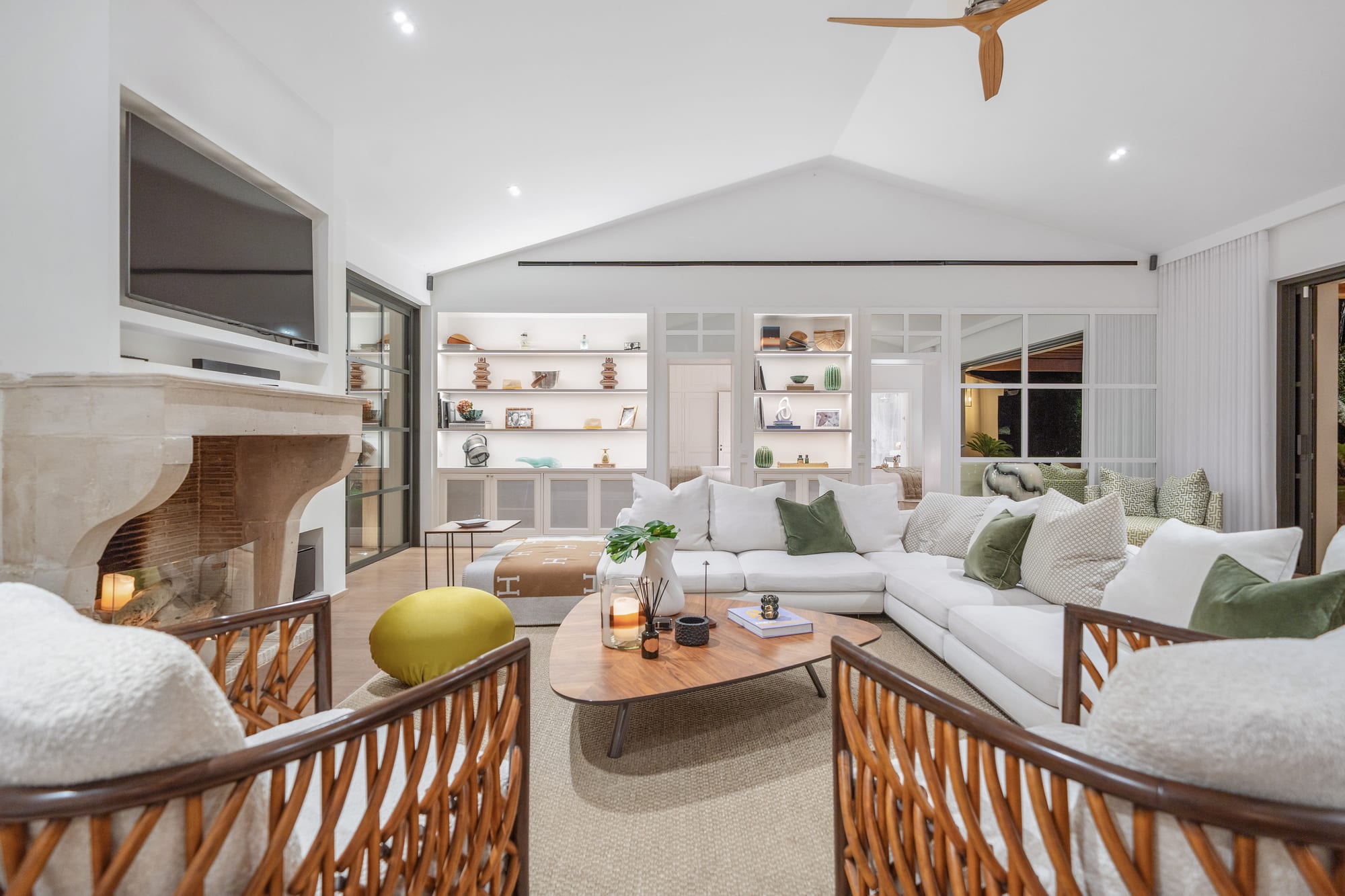 A sitting room with a stone fireplace, built-in shelving and pale sofas under a vaulted ceiling.