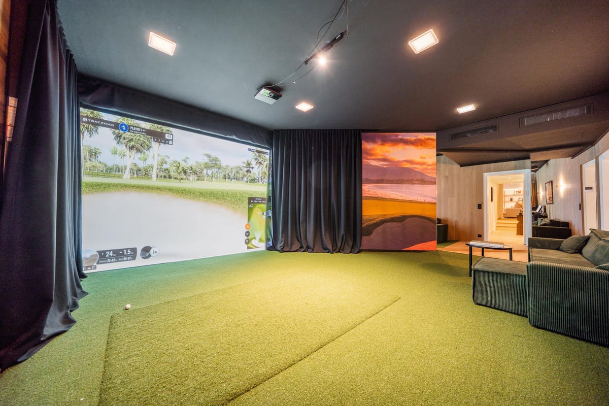 A golf simulator room: a wide projection screen showing a fairway, a putting surface underfoot and a sofa along the back wall.