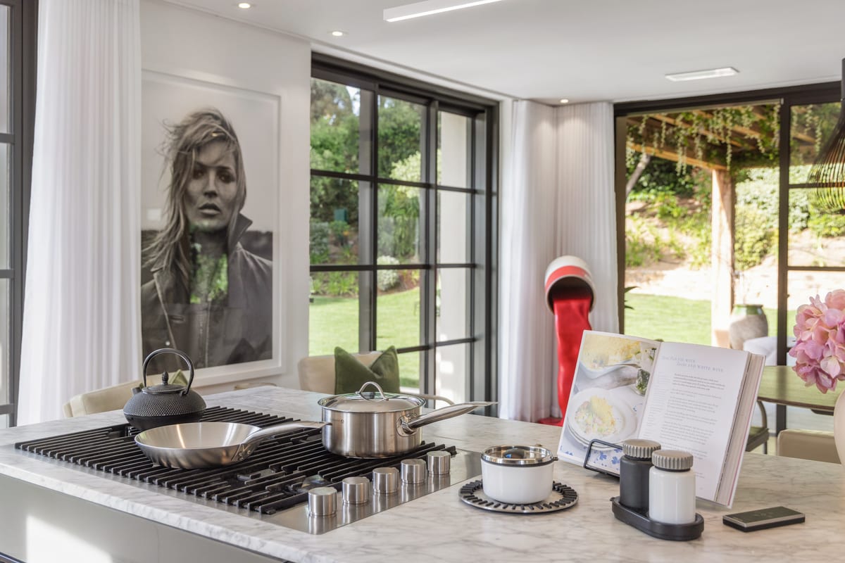 A kitchen island with a gas hob, a large portrait on the wall and glazed doors to the garden.