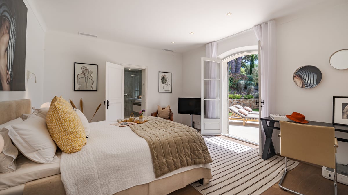 A bedroom with a desk under the window and doors open onto the terrace.