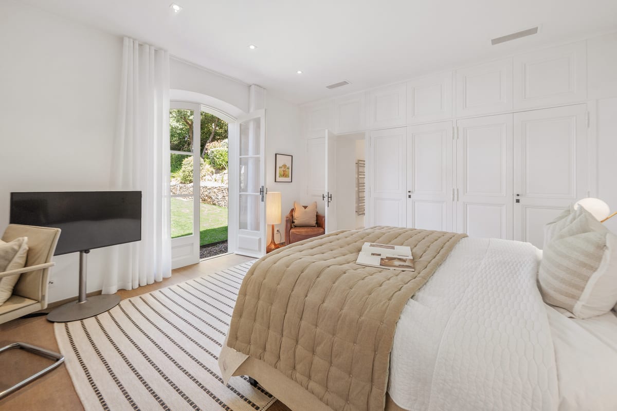 A bedroom with a striped rug and French doors standing open onto the garden.