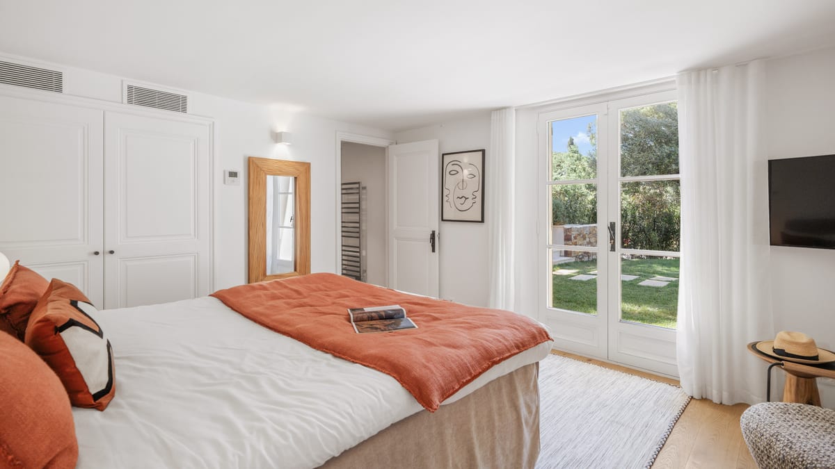 A bedroom with a terracotta throw across the bed and doors to the garden.