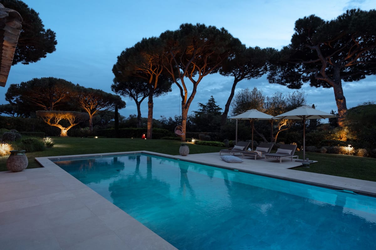 The pool in full sun, umbrella pines above it and the sea visible between the trunks.