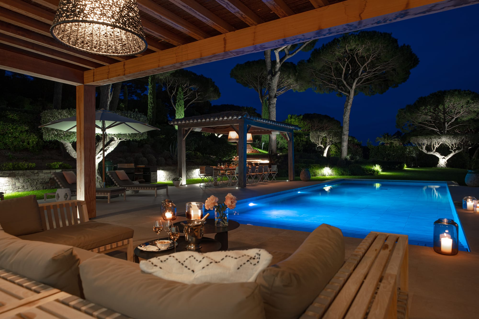 The timber pergola and the lit pool at blue hour, seen from the garden.