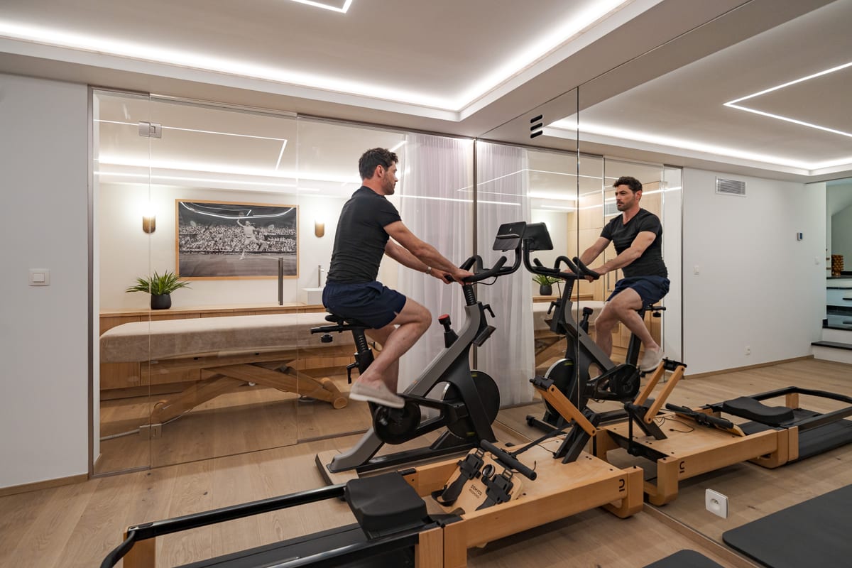 A gym room panelled in pale timber, with an exercise bike, weights along the wall and a full-height mirror.