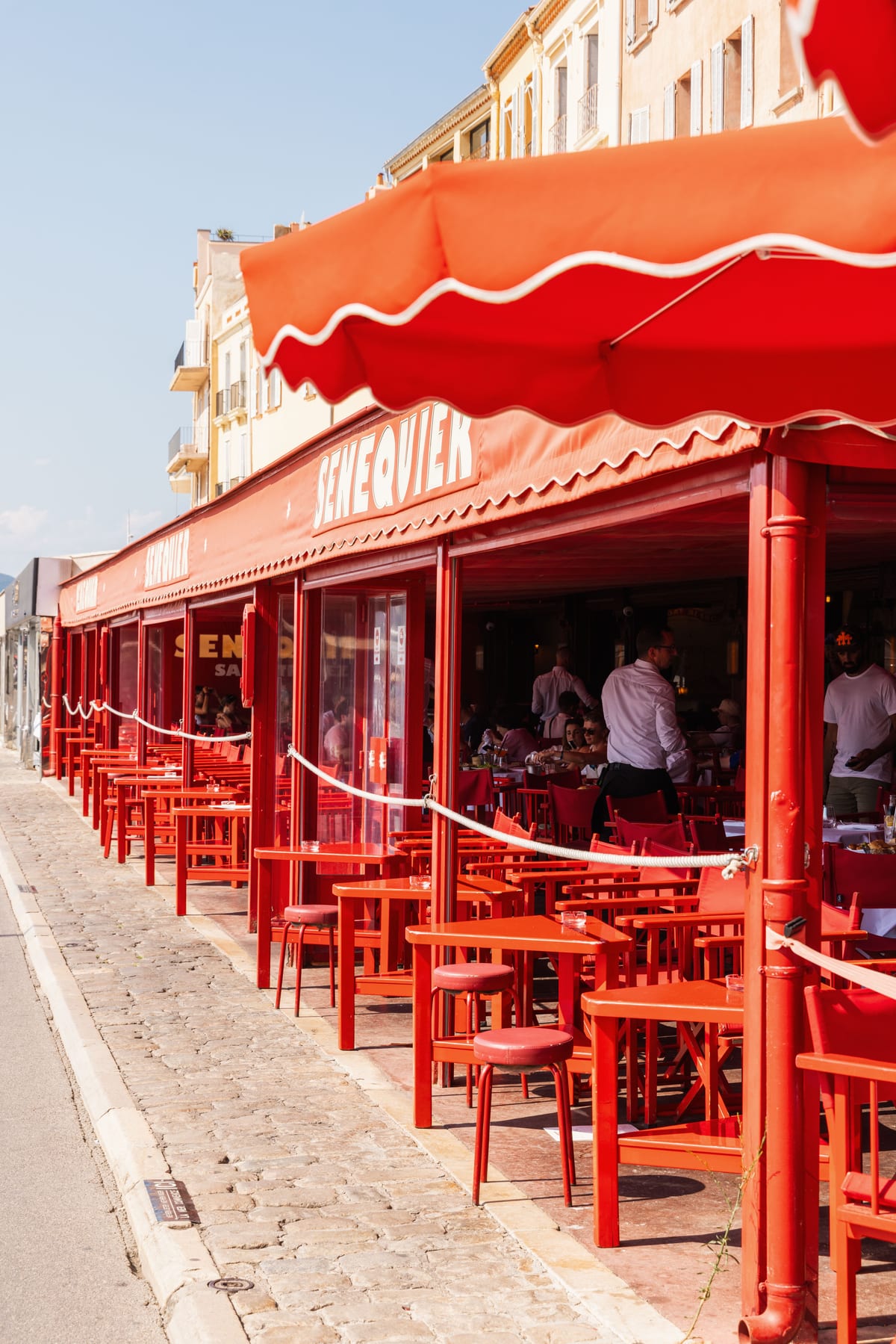 A long red awning over rows of red chairs and tables on the quayside terrace of the Senequier cafe.