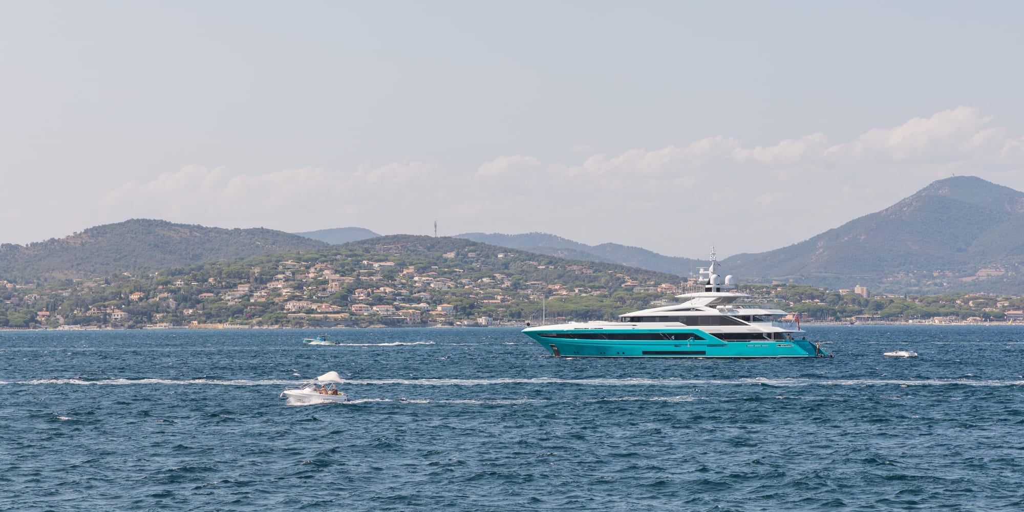 The gulf seen from the water, the wooded hills of the Maures along the far shore, a motor yacht crossing.