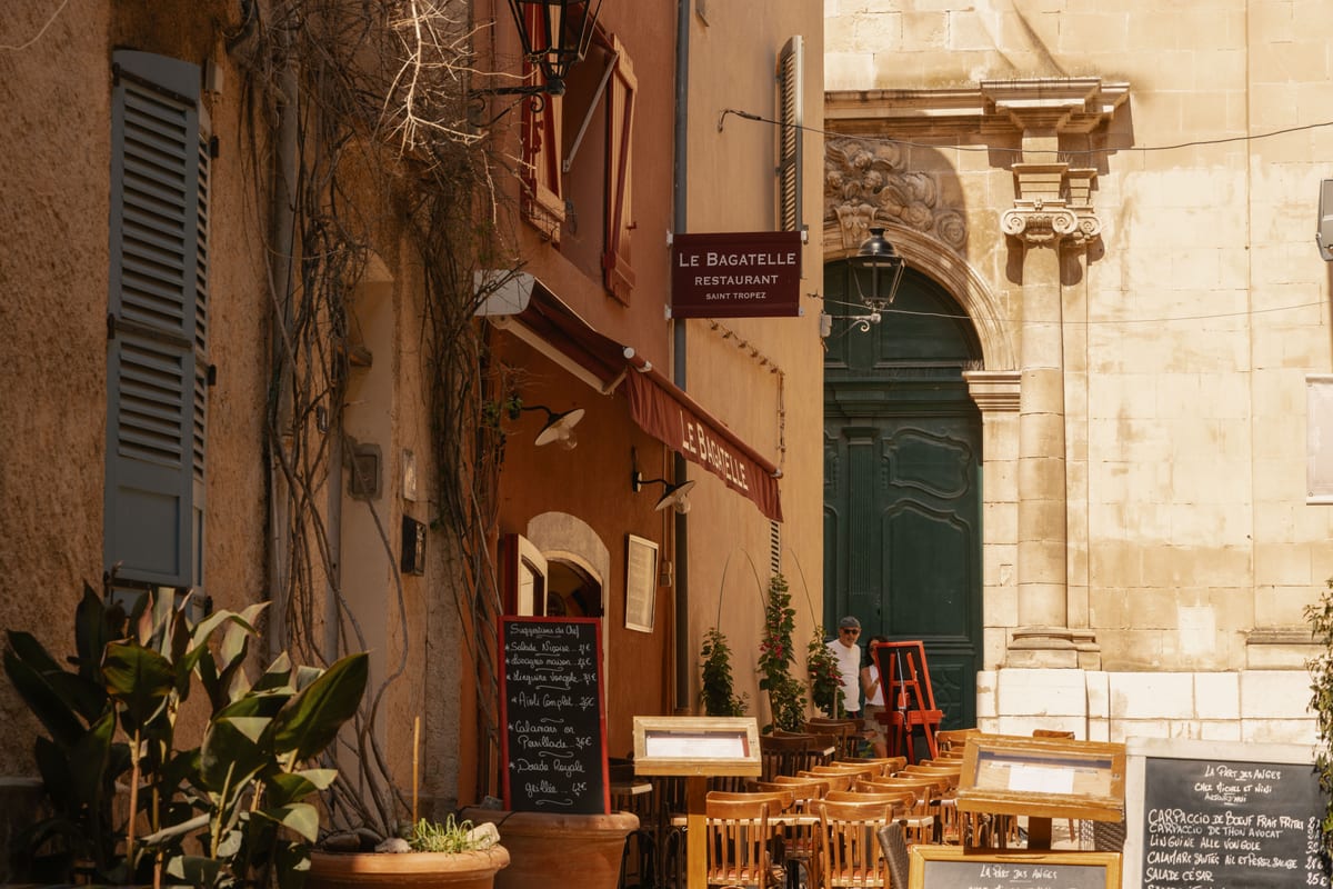 A corner of the old town: shuttered stone facades, a small restaurant terrace and a chalkboard menu in the shade.